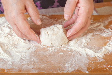 Female hands sculpt a bunch of raw dough on a wooden board with flour. Close-up