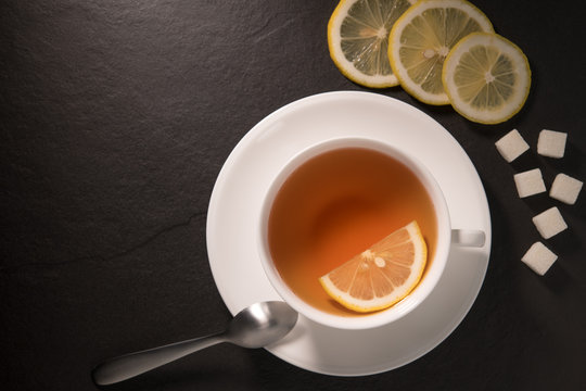Top view image of a cup of tea with lemon on black granite background