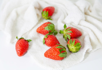 Fresh strawberry with green leaves scattered on white cloth isolated on white background. Selective focus. Delicious and healthy fruit.