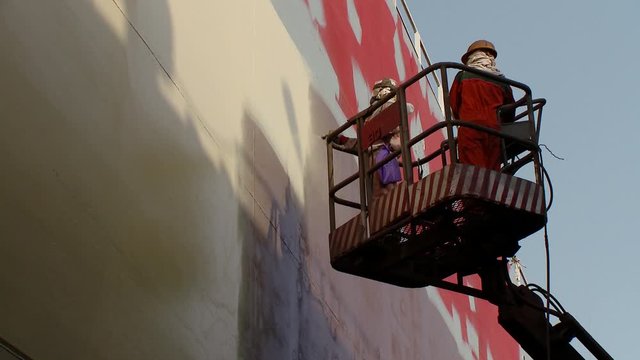 Two workers on a cherry-picker spray painting a side of an oil supertanker in dry dock in Bahrain