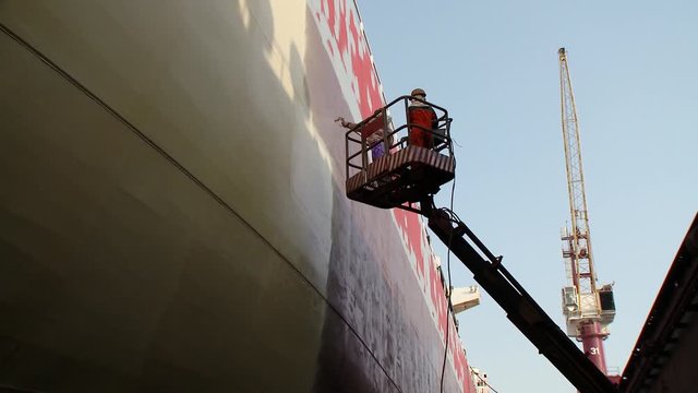 Two workers on a cherry-picker spray painting a side of an oil supertanker in dry dock in Bahrain