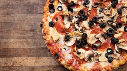 Pizza topped with olives, mushrooms, pepperoni and cheese atop a decorative cutting board.