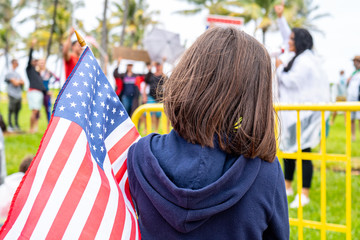 USA flag and child on demonstration. Little patriot. Girl with the American flag. American children. A child protests against coronavirus restrictions. Miami protesters. Civil liberties. Democracy.