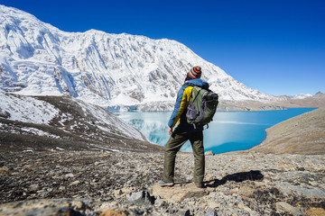 Travel and hikking concept: Trekker with backpack on Tilicho lake. Its 4900m above sea level. Snowly peaks of mountains and Tilicho lake on background. - obrazy, fototapety, plakaty