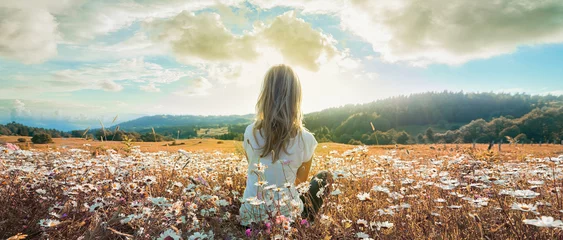 Fotobehang Slaapkamer Woman sitting on the chamomiles field and looking at the cloudy sky at sunset. Banner edition..  © upslim