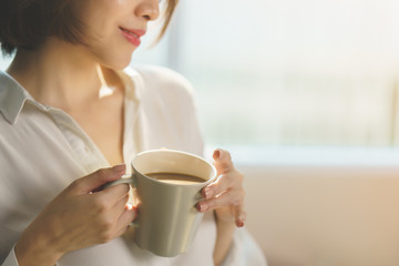 Woman hands holding hot cup of coffee or tea in morning sunlight.