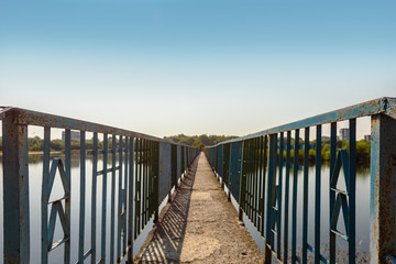 Old metal footpath bridge on river over blue sky background