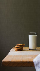 A simple rustic breakfast with a glass of fresh milk and cookies lies in a stack on a rustic wooden table.