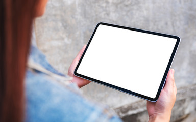 Mockup image of a woman holding a black tablet pc with blank white screen in the outdoors street background