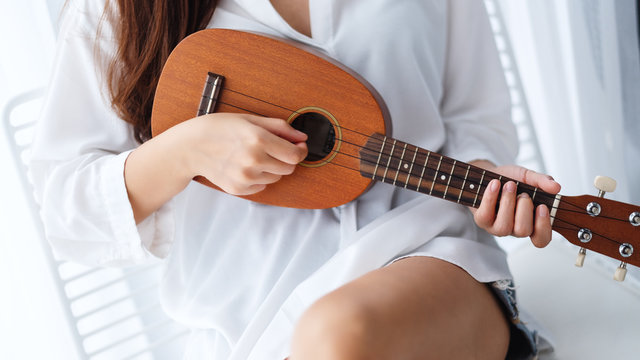 Closeup image of a woman sitting and playing ukulele in bedroom