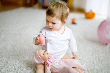 Lovely cute beautiful little baby girl playing with toy doll at home or nursery. Happy healthy...