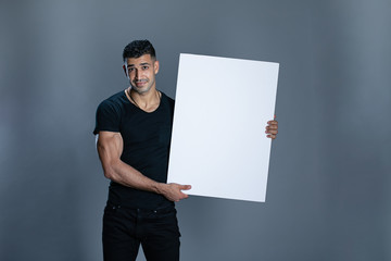 A fit handsome man holding a white board  in grey background