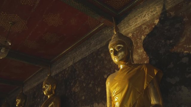 Beautiful golden Thai Buddha images sunset at Wat Suthat. Row of Buddha statues in a dark hall.
