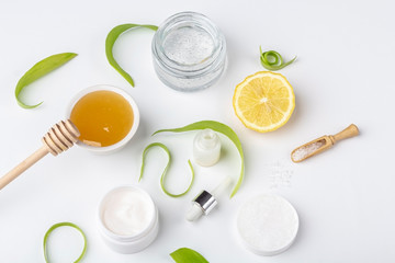 Natural organic ingredients to make home skin care. Cleansing and nourishing cosmetics. Beauty products: cream, honey, sea salt among green leaves on white background. Close up, copy space for text