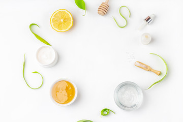 Natural organic ingredients to make home skin care. Cleansing and nourishing cosmetics. Beauty products: cream, honey, sea salt among green leaves on white background. Flat lay, copy space for text