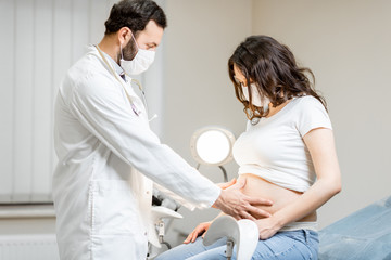 Obraz premium Doctor with a pregnant woman in medical masks during an examinations. Concept of new rules for the use of masks in medicine after or during a pandemic