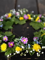 Spring floral grassy background. Wreath of fresh plant leaves with spring forest flowers laid out on a wooden dark table.