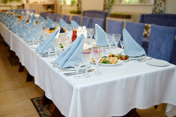Table setting with plates, blue napkins, wineglasses and cutlery on long table, copy space. Place setting at wedding reception. Table served for banquet in restaurant
