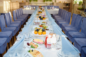 Table setting with plates, blue napkins, wineglasses and cutlery on long table, copy space. Place setting at wedding reception. Table served for banquet in restaurant