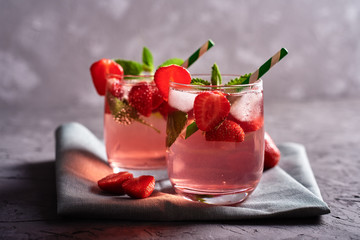 Fresh strawberry lemonade with ice, mint and paper straw in sparkling glasses on gray table background, copy space. Cold summer drink. Berry cocktail