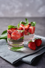 Water with strawberry and mint in sparkling glasses on gray napkin on concrete table, copy space. Cold summer drink. Mineral water
