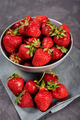 Red ripe strawberry in ceramic bowl on linen table napkin on gray concrete background, copy space. Healthy food concept, still life