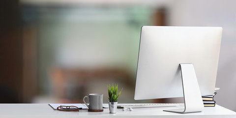 Workspace computer putting on white working desk and surrounded by coffee cup, clipboard, potted...