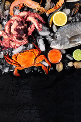 Fish and seafood, on overhead shot on a black background with a place for text. Sea bream. shrimps, crab, clams and caviar