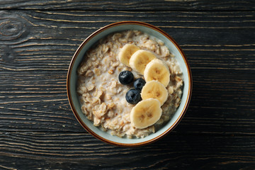 Bowl with oatmeal porridge and fruits on wooden background