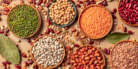 Legumes assortment, a flat lay panorama on a brown background. Lentils, soybeans, chickpeas, red...