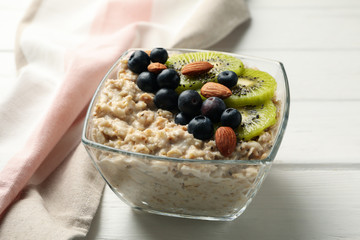 Towel and bowl with oatmeal porridge and fruits on wooden background