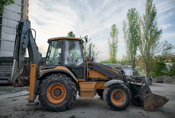 Parked tractor on the wheels with bucket on the city street