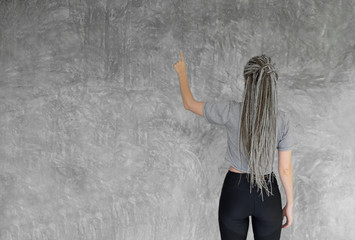 Back view of female person in gray shirt  show point on gray wall background
