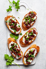 Toasts with sun-dried tomatoes and cream cheese on white board, white background, top view.