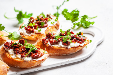 Toasts with sun-dried tomatoes and cream cheese on white board, white background.