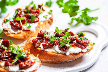 Toasts with sun-dried tomatoes and cream cheese on white board, white background.