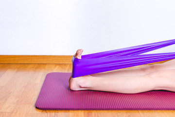 detail of caucasian woman stretching calves with a purple gym elastic band