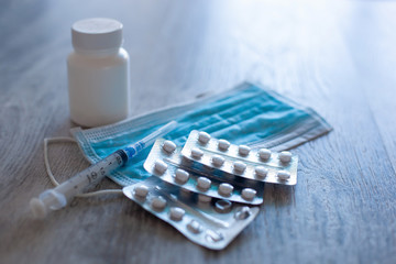 Medications in form of tablets, protective medical mask and syringe on table.