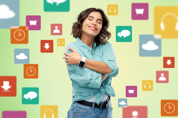 self loving, care and people concept - portrait of happy smiling young woman in turquoise shirt with smart watch hugging herself over app icons on green background