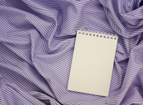 paper notebook with an empty cover on a purple-striped tablecloth.