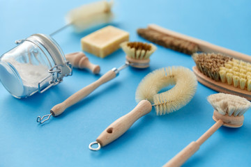 natural cleaning stuff, sustainability and eco living concept - different brushes and soda powder with wooden scoop in glass jar on blue background