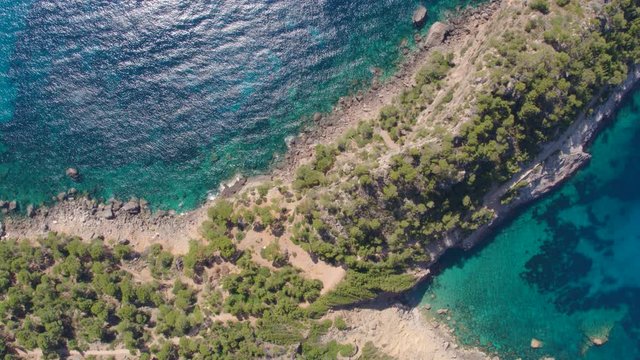 AERIAL DRONE TOP DOWN ZENITHAL SMOOTH SIDE SHOT OF MEDITERRANEAN CLIFFS AND PENINSULA, ROCKY SEA SIDE WITH BLUE TURQUOISE WATER AND GREEN PINE FOREST