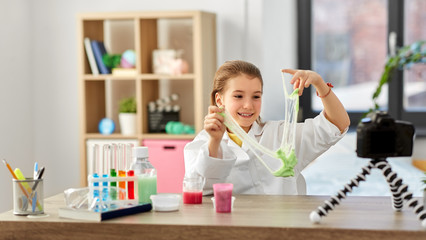 science, childhood and blogging concept - happy smiling little girl blogger with slime and camera...