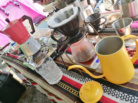 Alternative coffee brewing outdoors in travel. Steel kettle, hot coffee in cup, coffee dripper, geyser maker, glass flask with filter on background 