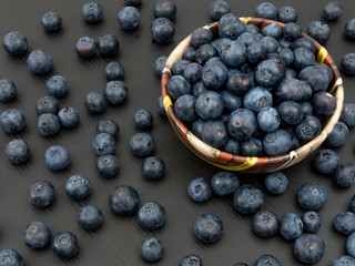 Blueberries in a ceramic bowl and on a black wooden table. Healthy blueberry snack. Fresh vegan breakfast. Close up. Bunch of vitamins.