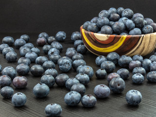 Blueberries in a ceramic bowl and on a black wooden table. Healthy blueberry snack. Fresh vegan breakfast. Close up. Bunch of vitamins.