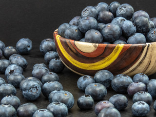 Blueberries in a ceramic bowl and on a black wooden table. Healthy blueberry snack. Fresh vegan breakfast. Close up. Bunch of vitamins.
