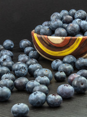 Blueberries in a ceramic bowl and on a black wooden table. Healthy blueberry snack. Fresh vegan breakfast. Close up. Bunch of vitamins.
