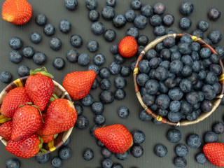 Blueberries and Strawberries in ceramic bowls and on a black wooden table. Healthy red berry snack. Fresh vegan breakfast. Close up. Bunch of vitamins.