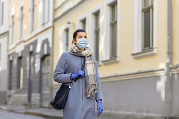 Fototapeta premium health, safety and pandemic concept - young woman wearing protective medical mask on empty street of old town in tallinn city